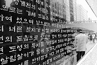 Se ve una pared en una calle, con muchas líneas o flujos de escritura en caracteres parecidos a los coreanos, japoneses o chinos.