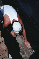 Un albañil con casco blanco y camiseta de tirantes blanca, construye un muro con ladrillos.