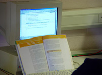 Pantalla de un ordenador con un libro abierto en primer plano.