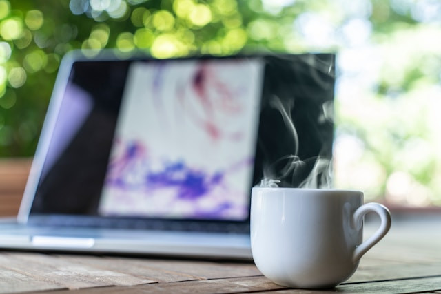 Una taza de café humeante frente a un portátil.
