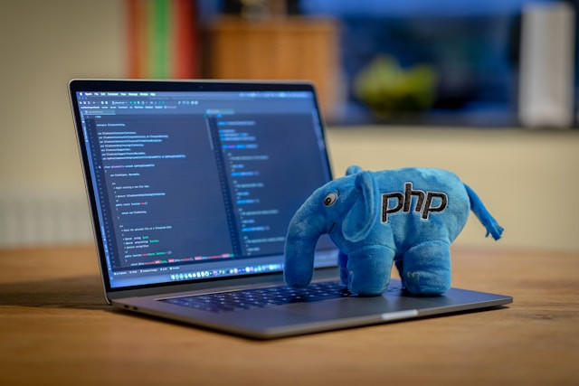 Peluche de elefante PHP junto a un portátil con código en pantalla.