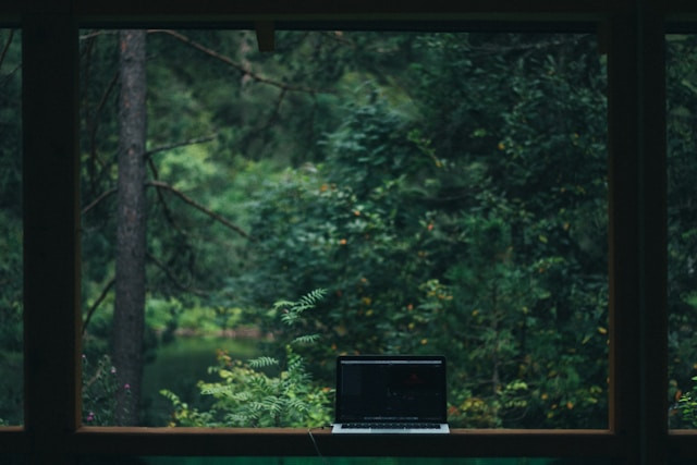 Portátil abierto en una ventana con vista al bosque.