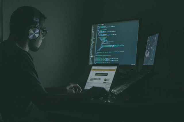 Hombre programando actualizaciones de seguridad contra XSS en múltiples monitores.