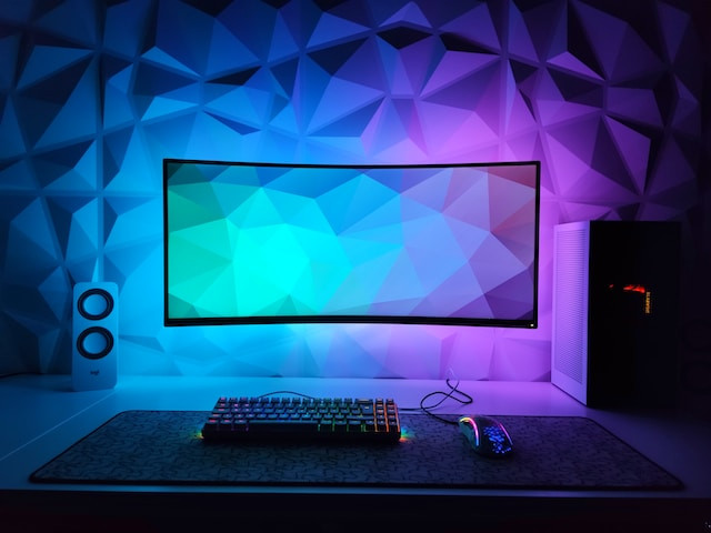 Torre y monitor grande en una habitación iluminada en color azúl y púrpura.