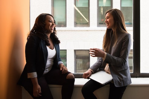 Dos mujeres enfrente de una ventana sonriendo.