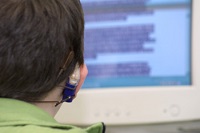 Aula de informática con estudiante atento a las indicaciones del libro de texto y con el ordenador delante.