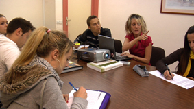 Reunión Equipo de varias personas alrededor de una mesa, sobre la que hay un proyector que una persona está usando para una presentación.